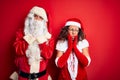 Middle age couple wearing Santa costume and glasses over isolated red background Tired hands covering face, depression and Royalty Free Stock Photo