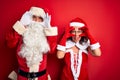 Middle age couple wearing Santa costume and glasses over isolated red background Trying to open eyes with fingers, sleepy and Royalty Free Stock Photo