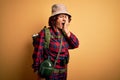 Middle age curly hair hiker woman hiking wearing backpack and water canteen using binoculars Yawning tired covering half face, eye