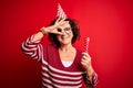 Middle age curly hair woman wearing birthday funny hat holding party trumpet on celebration with happy face smiling doing ok sign Royalty Free Stock Photo