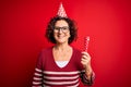 Middle age curly hair woman wearing birthday funny hat holding party trumpet on celebration with a happy face standing and smiling Royalty Free Stock Photo
