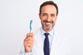 Middle age dentist man holding toothbrush standing over isolated white background with a happy face standing and smiling with a