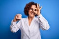 Middle age dentist woman wearing coat holding plastic denture teeth over blue background with happy face smiling doing ok sign Royalty Free Stock Photo