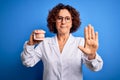 Middle age dentist woman wearing coat holding plastic denture teeth over blue background with open hand doing stop sign with