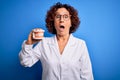Middle age dentist woman wearing coat holding plastic denture teeth over blue background scared in shock with a surprise face,
