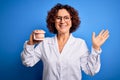 Middle age dentist woman wearing coat holding plastic denture teeth over blue background very happy and excited, winner expression Royalty Free Stock Photo