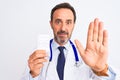 Middle age doctor man holding pills standing over isolated white background with open hand doing stop sign with serious and Royalty Free Stock Photo