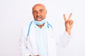 Middle age doctor man wearing stethoscope and mask over isolated white background smiling with happy face winking at the camera Royalty Free Stock Photo