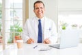 Middle age doctor man wearing white medical coat working with laptop at the clinic with a happy and cool smile on face Royalty Free Stock Photo