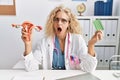 Middle age doctor woman holding birth control pills in shock face, looking skeptical and sarcastic, surprised with open mouth Royalty Free Stock Photo