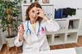 Middle age doctor woman holding electronic cigarette at medical clinic smiling happy doing ok sign with hand on eye looking Royalty Free Stock Photo