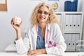 Middle age doctor woman holding piggy bank at the clinic looking positive and happy standing and smiling with a confident smile Royalty Free Stock Photo