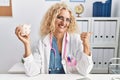 Middle age doctor woman holding piggy bank at the clinic pointing thumb up to the side smiling happy with open mouth Royalty Free Stock Photo