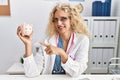 Middle age doctor woman holding piggy bank at the clinic smiling happy pointing with hand and finger Royalty Free Stock Photo