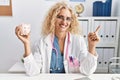 Middle age doctor woman holding piggy bank at the clinic smiling happy pointing with hand and finger to the side Royalty Free Stock Photo