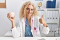 Middle age doctor woman holding piggy bank at the clinic smiling happy and positive, thumb up doing excellent and approval sign Royalty Free Stock Photo