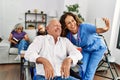 Middle age doctor woman and retired man sitting on wheelchair make selfie by the smartphone at nursing home Royalty Free Stock Photo