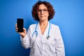 Middle age doctor woman wearing coat and stethoscope holding smartphone showing screen with a confident expression on smart face Royalty Free Stock Photo