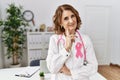 Middle age doctor woman wearing pink cancer ribbon on uniform looking confident at the camera smiling with crossed arms and hand Royalty Free Stock Photo