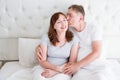 Middle age family couple in white bedroom in bed. Husband kiss wife. Love and romance. Healthy relationship.