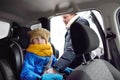 Middle age father helps his preschooler son fasten his seat belt on a car seat. Cute little child sitting in a car on a winter day Royalty Free Stock Photo