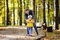 Middle age father showing his toddler son how to ride a scooter in a autumn park Royalty Free Stock Photo