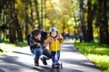 Middle age father showing his toddler son how to ride a scooter in a autumn park