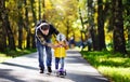 Middle age father showing his toddler son how to ride a scooter in a autumn park