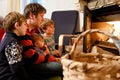 Middle age father sitting by fireplace with cute little baby girl and two kids boys at home. Happy family, dad with Royalty Free Stock Photo