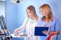 Middle age female dentist with assistance of young female nurse checking dental tools and instruments in dentist office Royalty Free Stock Photo