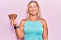 Middle age fit blonde woman holding bowl with almonds looking positive and happy standing and smiling with a confident smile Royalty Free Stock Photo