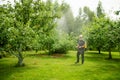 Middle age gardener with a mist fogger sprayer sprays fungicide and pesticide on bushes and trees. Protection of cultivated plants