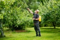 Middle age gardener with a mist fogger sprayer sprays fungicide and pesticide on bushes and trees. Protection of cultivated plants