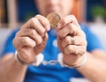 Middle age grey-haired man criminal holding litecoin crypto currency wearing handcuffs at home