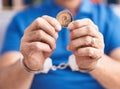 Middle age grey-haired man criminal holding polkadot crypto currency wearing handcuffs at home