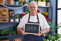 Middle age grey-haired man florist smiling confident holding open blackboard at florist