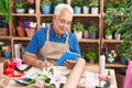 Middle age grey-haired man florist using touchpad writing on notebook at florist Royalty Free Stock Photo