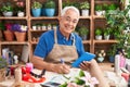 Middle age grey-haired man florist using touchpad writing on notebook at florist Royalty Free Stock Photo