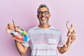 Middle age grey-haired man holding palette and manikin smiling and laughing hard out loud because funny crazy joke Royalty Free Stock Photo