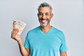 Middle age grey-haired man holding united kingdom pounds looking positive and happy standing and smiling with a confident smile