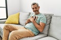 Middle age grey-haired man hugging picture sitting on sofa at home