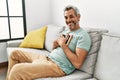 Middle age grey-haired man hugging picture sitting on sofa at home