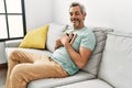 Middle age grey-haired man hugging picture sitting on sofa at home