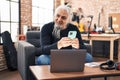 Middle age grey-haired man musician using smartphone sitting on chair at music studio