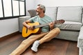 Middle age grey-haired man playing classical guitar sitting on floor at home Royalty Free Stock Photo