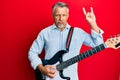 Middle age grey-haired man playing electric guitar doing rock sign depressed and worry for distress, crying angry and afraid