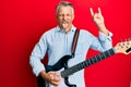 Middle age grey-haired man playing electric guitar doing rock sign sticking tongue out happy with funny expression Royalty Free Stock Photo