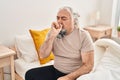 Middle age grey-haired man sitting on bed coughing at bedroom Royalty Free Stock Photo