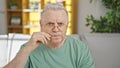 Middle age grey-haired man sitting on sofa doing close mouth gesture at home