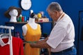 Middle age grey-haired man tailor measuring dress at tailor shop